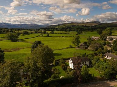 A rural landscape with green fields trees and houses under a partly cloudy sky at March House in Windermere