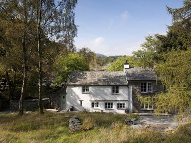 A stone and white plaster house surrounded by trees and grass at Wythebank in Langdale
