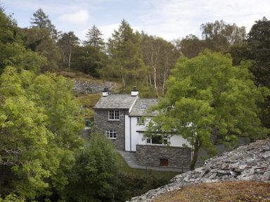 Stone and white house surrounded by trees and rocky landscape at Wythebank in Langdale