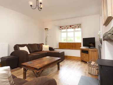 A living room with brown sofas a wooden coffee table a wooden cabinet with a television and a window seat at Wythebank in Langdale