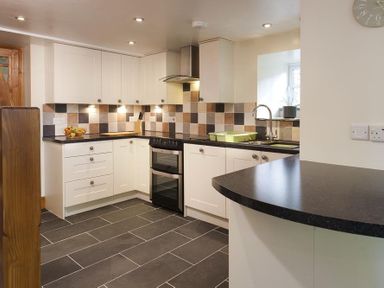 A kitchen with white cabinets a black countertop a built in oven tiled backsplash and a sink at Wythebank in Langdale