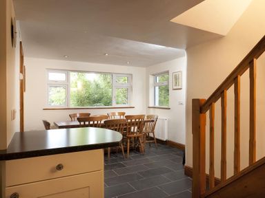 A dining area with a wooden table and chairs near windows beside a staircase at Wythebank in Langdale