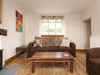 A living room with a brown sofa with cushions a wooden coffee table a window with patterned curtains and a painting on the wall at Wythebank in Langdale