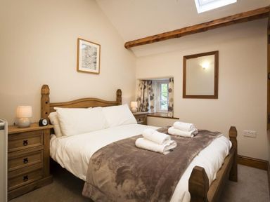 A bedroom with a wooden bed frame bedside tables lamps mirror and a small window at Wythebank in Langdale