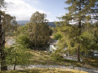 A small white house surrounded by trees and greenery in a rural area at Wythebank in Langdale