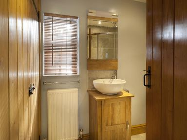 A bathroom with a wooden vanity unit a round basin a mirror a window with blinds and a radiator at Wythebank in Langdale
