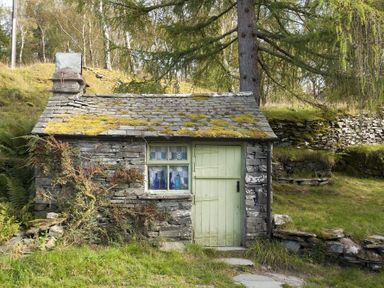 A small stone cottage with a moss-covered roof and a green door in a grassy area at Wythebank in Langdale