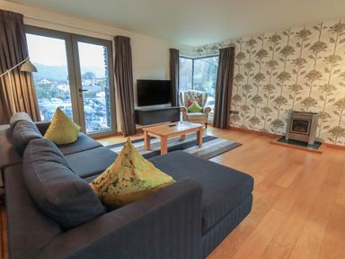 A living room with blue sofa green pillows wooden coffee table armchair and a stove at Idle Mill 1 in Ambleside