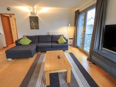 A living room with a grey sofa with green cushions a wooden coffee table and a TV at Idle Mill 1 in Ambleside