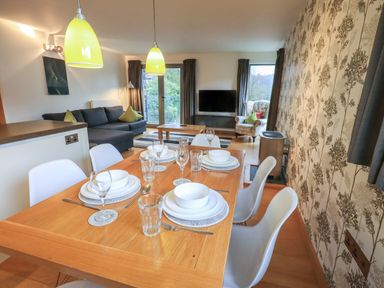 A dining table set with plates, bowls, glasses, and cutlery in an open-plan living room with a sofa, armchair, TV, and patterned wallpaper at Idle Mill 1 in Ambleside