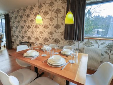 A dining table set with plates bowls glasses and cutlery in a room with patterned wallpaper and large window at Idle Mill 1 Ambleside