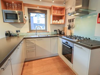 A kitchen with white cabinets black countertops a window a gas stove oven microwave sink and wooden shelves at Idle Mill 1 Ambleside