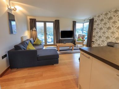A living room with a dark sofa green cushions a wooden coffee table a TV and an armchair near windows at Idle Mill 1 in Ambleside