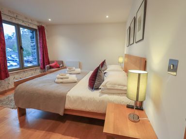 A bedroom with a double bed two folded towels bedside table lamps and a window with red curtains at Idle Mill 1 Ambleside