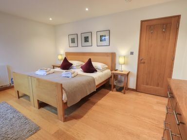 A bedroom with a wooden double bed with pillows and towels bedside tables with lamps a wooden door and a chest of drawers at Idle Mill 1 in Ambleside