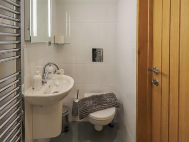 A small bathroom with a sink a wall-mounted toilet a wooden door and a metal towel rail at Idle Mill 1 in Ambleside