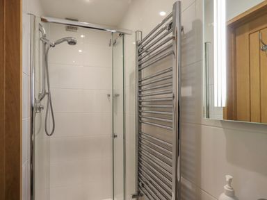 A bathroom with a shower area, glass door, chrome towel heater, and a mirror at Idle Mill 1 in Ambleside