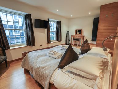 A bedroom with a double bed two windows a wall-mounted TV and a wooden dressing table at Idle Mill 1 in Ambleside
