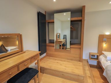 A bedroom with a wooden dressing table bench open wardrobe with mirror and a bed at Idle Mill 1 in Ambleside