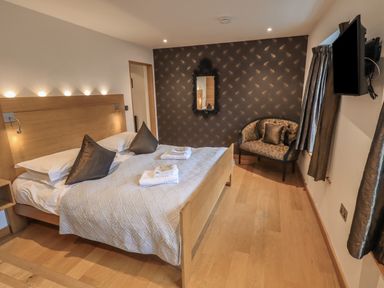 A bedroom with a double bed, pillows, folded towels, a wall mirror, a small sofa, and a wall-mounted television at Idle Mill 1 in Ambleside