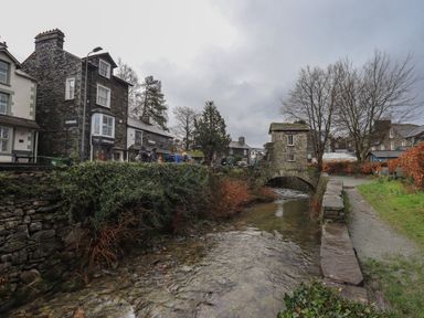 Stone buildings and shops along a river with a stone arch bridge and a walkway at Idle Mill 1 in Ambleside