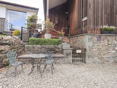 An outdoor seating area with two metal chairs and a round table next to stone steps and a wooden building at Le Chalet in Elterwater