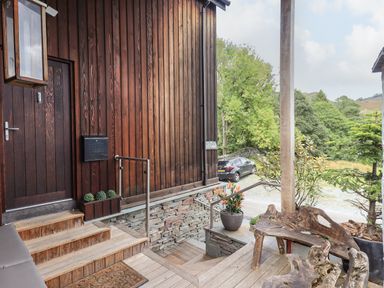 A wooden porch with steps and rustic wooden chairs next to a plant and a car outside at Le Chalet in Elterwater