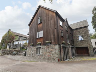A stone and wood exterior of a multi-story house with windows and flower boxes at Le Chalet in Elterwater