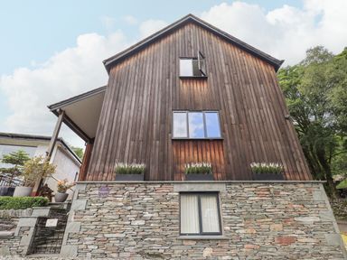 The exterior of a building with wooden upper walls and stone lower walls with plants in pots at Le Chalet in Elterwater