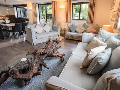 A living room with sofas cushions a unique wooden coffee table dining area and windows at Le Chalet in Elterwater