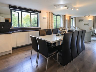 A dining area with black chairs and a white table next to windows and a kitchen countertop at Le Chalet in Elterwater