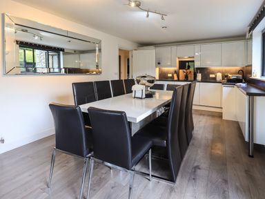 A dining area with a long white table surrounded by black chairs next to a kitchen with white cabinets at Le Chalet in Elterwater