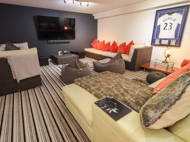 A TV mounted on a wall with sofas bean bags and a framed sports jersey in a living room at Le Chalet in Elterwater