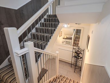 A stairwell with striped carpet and a wine rack below a large mirror at Le Chalet in Elterwater