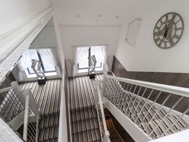 A staircase with striped carpet a large wall mirror a window with sheer curtains and a metal sculpture at Le Chalet in Elterwater