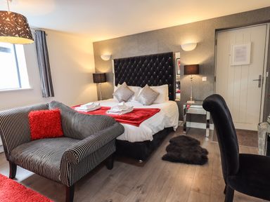 A bedroom with a double bed with white and red bedding a striped armchair with a red pillow and a black chair at Le Chalet in Elterwater