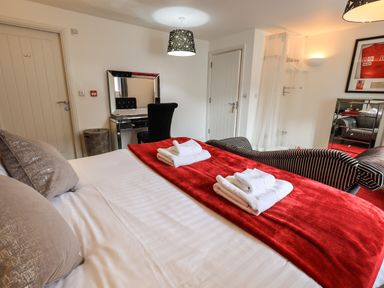 A bedroom with a bed a red runner and folded towels a desk with a chair and a mirror at Le Chalet in Elterwater