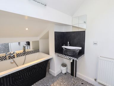 A bathroom with a black bathtub a black sink on a black countertop and black and white checkered floor at Le Chalet in Elterwater