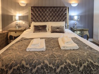 A bedroom with a double bed, two bedside tables with lamps, and folded towels on the bed at Le Chalet in Elterwater