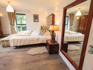 A bedroom with a bed side table lamps large mirror wooden wardrobe and window with curtains at Le Chalet in Elterwater