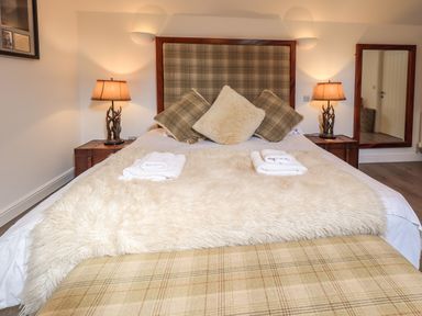 A bedroom with a bed with multiple pillows and folded towels on a fur blanket at Le Chalet in Elterwater