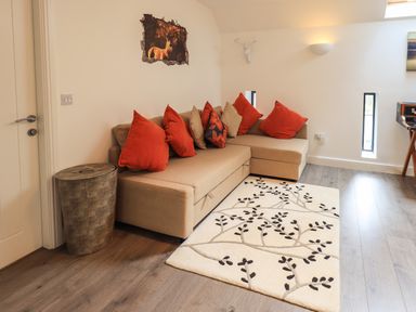 A living room with a beige sectional sofa with red and brown cushions a patterned rug on wooden floor and a wall decoration of a deer at Le Chalet in Elterwater