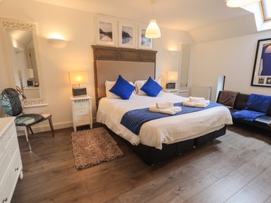 A bedroom with a double bed blue pillows white towels bedside tables and a sofa at Le Chalet in Elterwater