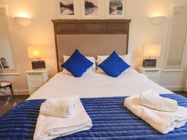A bedroom with a bed with blue pillows white towels on a blue bed runner bedside tables with lamps at Le Chalet in Elterwater
