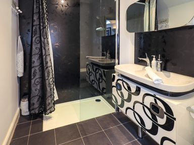 A bathroom with a sink cabinet and a walk-in shower with a patterned curtain at Le Chalet in Elterwater