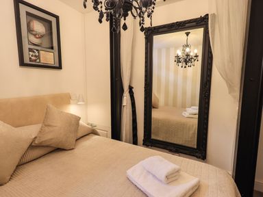 A bedroom with a beige bedspread and pillows a large black framed mirror and a chandelier at Le Chalet in Elterwater