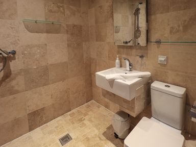 A bathroom with a sink mirror towel toilet trash bin and tiled walls and floor at Le Chalet in Elterwater