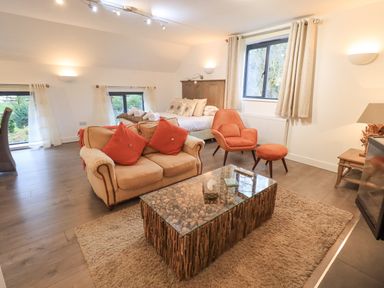 A living area with a beige sofa with red pillows an orange armchair with ottoman a bed a wooden coffee table with a glass top and windows with curtains at Le Chalet in Elterwater