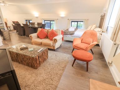 A living room and bedroom area with a beige loveseat with red cushions a glass coffee table with wood sticks and an orange armchair and ottoman at Le Chalet in Elterwater