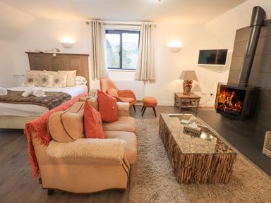 A living area with a sofa and armchair near a fireplace and a bed by a window at Le Chalet in Elterwater